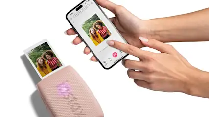 Una persona usa un telefono per stampare una foto su una stampante rosa. La foto mostra due persone.