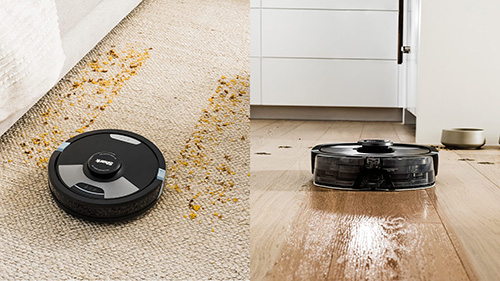 Aspirapolveri robot neri su moquette beige e parquet lucido, con briciole sparse e porta bianca in secondo piano.