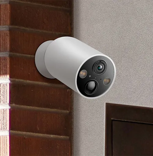 Telecamera di sicurezza cilindrica bianca montata su parete accanto a mattoni e legno scuro.