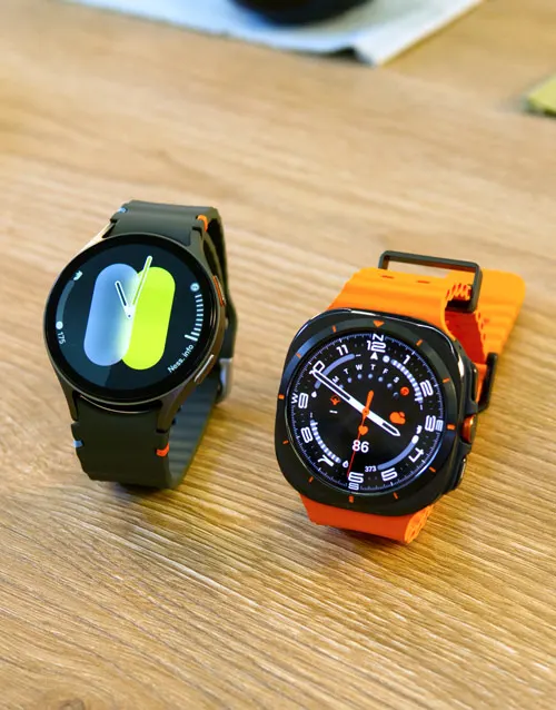 Due orologi su un tavolo di legno. Uno è nero con un display digitale verde e bianco. L'altro è arancione con un quadrante analogico.