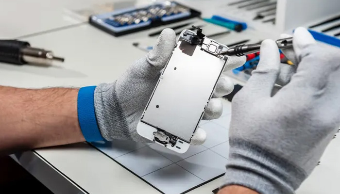 Riparazione di un telefono: mani con guanti grigi usano cacciavite su un telefono bianco aperto. Sul tavolo utensili e accessori.
