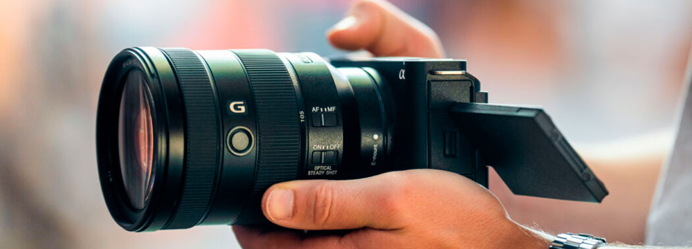 Un uomo tiene una fotocamera nera con un grande obiettivo e uno schermo esteso.