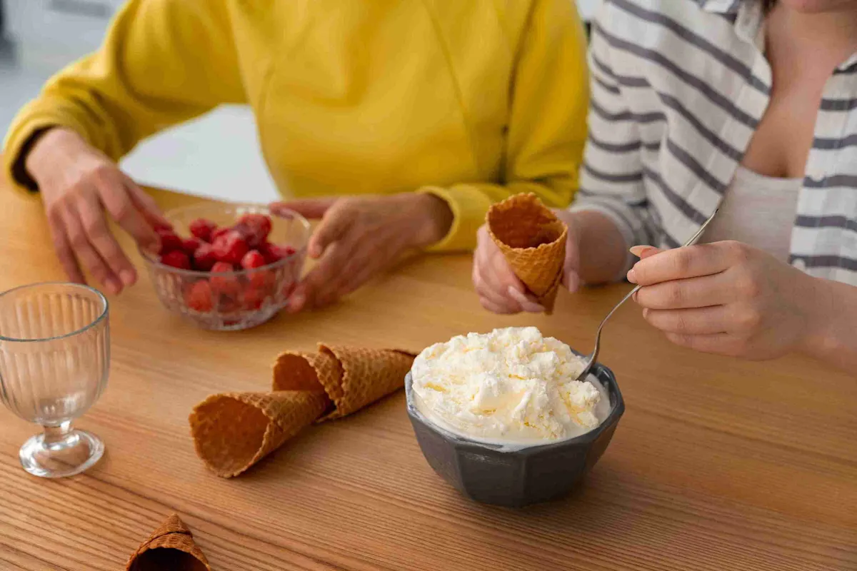 Persone preparano coni gelato su un tavolo di legno. Ci sono fragole, gelato, coni e una ciotola vuota.