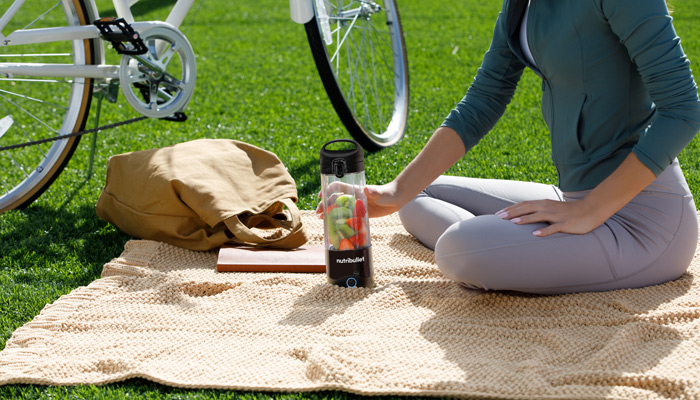 Donna seduta su una coperta sull'erba con frullatore, borsa e bici.
