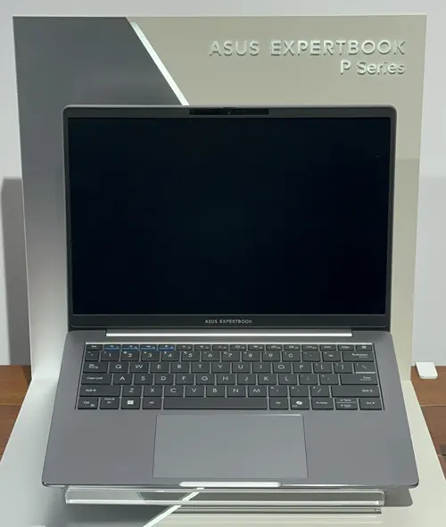 Notebook ASUS ExpertBook aperto, schermo nero, tastiera grigia. Sfondo con logo del prodotto. Cavo di alimentazione visibile.