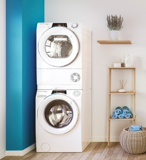 Lavanderia con lavatrice e asciugatrice bianche impilate, scaffale di legno con asciugamani e cesto in vimini.