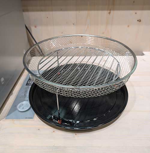 Una griglia rotonda in metallo sopra una teglia nera su un piano di lavoro in legno chiaro.