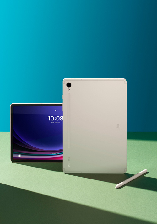 Due tablet su tavolo verde con sfondo blu. Uno mostra l'ora 10:08 e l'altro ha una fotocamera. Penna a destra.