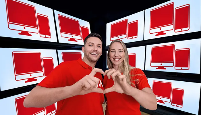 Uomo e donna sorridono, mani a forma di cuore. Sfondo con schermi che mostrano icone rosse di computer e smartphone.