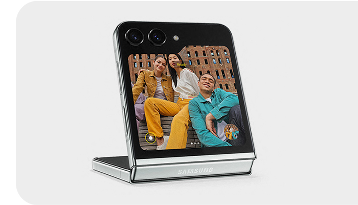 Smartphone pieghevole aperto, schermo mostra tre persone sedute su una panchina con un edificio sullo sfondo.