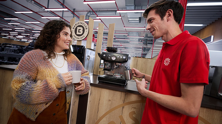 due persone davanti all'area caffè di mediaworld ridono e bevono un caffè