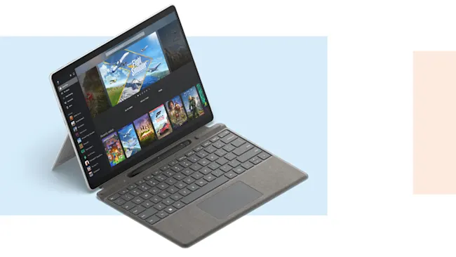 Tablet grigio con tastiera collegata, appoggiato su supporto, schermo acceso con immagini di videogiochi.