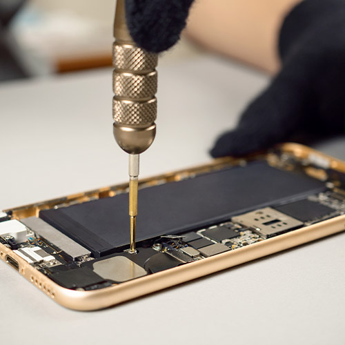 Un tecnico ripara un telefono dorato aperto con batteria nera, usando un cacciavite con manico zigrinato.