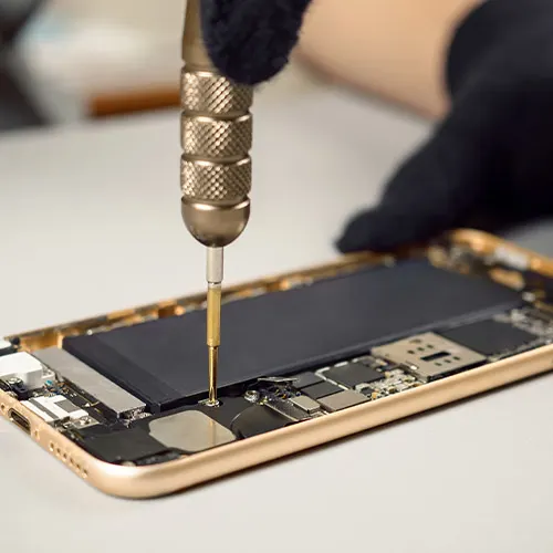 Un tecnico ripara un telefono dorato aperto con batteria nera, usando un cacciavite con manico zigrinato.