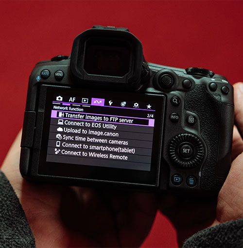 Fotocamera nera mostra un menu su uno schermo LCD, tenuta da due mani su sfondo rosso.
