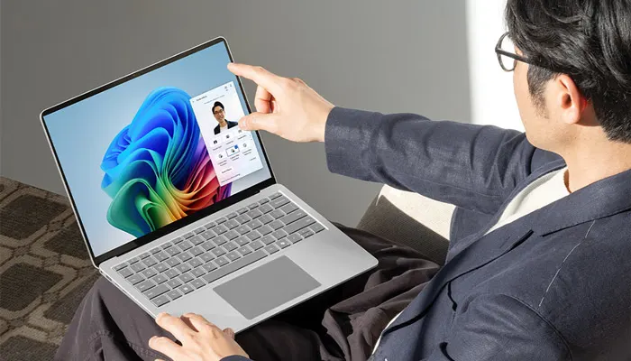 Uomo con occhiali usa un laptop con sfondo colorato. Una finestra pop-up mostra un profilo. L'uomo indossa una giacca blu.