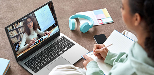 Donna scrive su un quaderno vicino a un laptop. Sullo schermo del laptop c'� una videochiamata con una donna e una libreria.