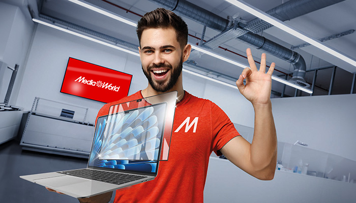 Uomo sorridente con maglietta rossa che mostra un laptop. Sullo sfondo, insegna verde "Better Way" e soffitto con tubature.