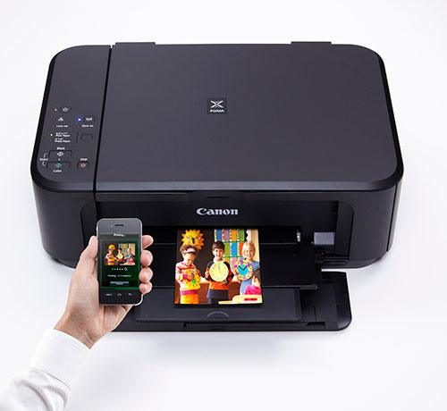 C'� una stampante nera Canon, una foto stampata e un telefono in una mano. Lo sfondo � bianco.