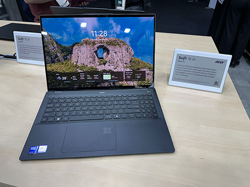 Un portatile aperto mostra un paesaggio montano con cielo azzurro. L'ora digitale è 11:28. Due cartelli bianchi sono sul tavolo.