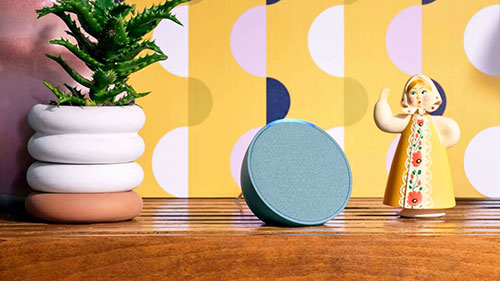 Natura, speaker blu e statuina su tavolo in legno. Sullo sfondo, carta da parati gialla con pois bianchi e semicerchi blu.