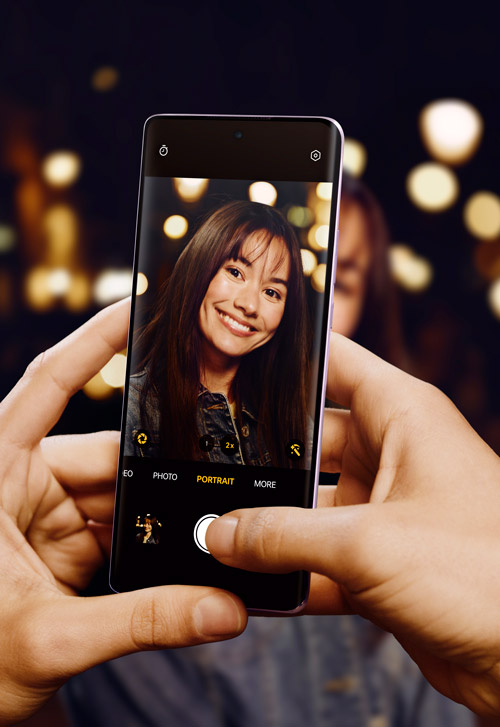 Mani che tengono un telefono che mostra una foto di una donna sorridente su uno sfondo scuro con luci sfocate.