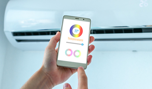 Una mano tiene un telefono con uno schermo che mostra una temperatura di 22 gradi. Sullo sfondo � presente un condizionatore d'aria.