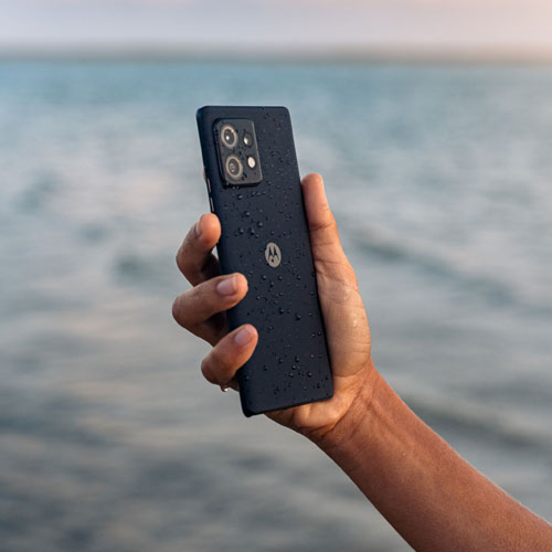 Una mano tiene un telefono nero con gocce d'acqua. Sullo sfondo C'� il mare.