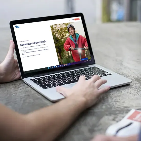 Un laptop aperto mostra il sito MediaWorld. Una mano digita sulla tastiera. Sul tavolo c'è una brochure.