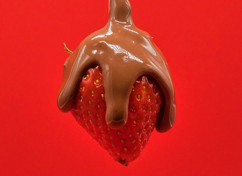 Fragola rossa ricoperta di cioccolato fuso marrone su sfondo rosso.