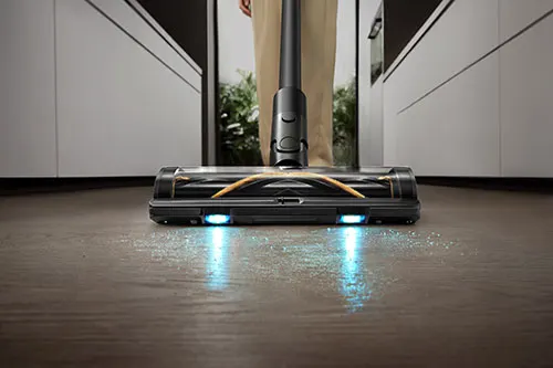 Primo piano di un aspirapolvere nero su un pavimento di legno, con mobili bianchi sullo sfondo.