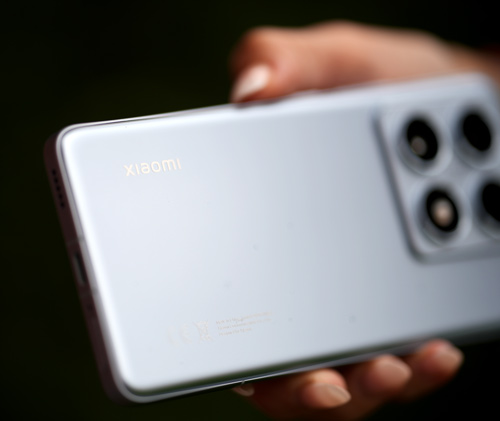 Mano che tiene un telefono grigio chiaro con quattro obiettivi circolari e il marchio del produttore su sfondo scuro.