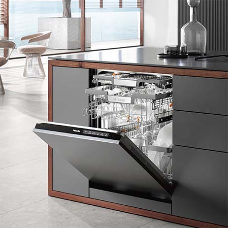 Lavastoviglie aperta, piena di stoviglie, in una cucina moderna con mobili grigi e dettagli in legno.