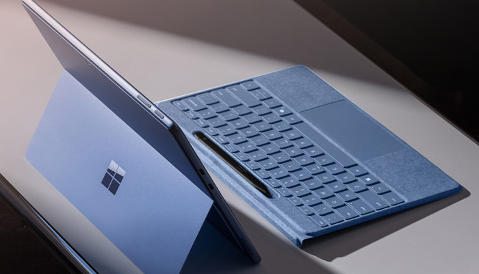 Un computer portatile blu è appoggiato su un tavolo. Una penna è appoggiata sulla tastiera. Sul retro c'è il logo di Windows.