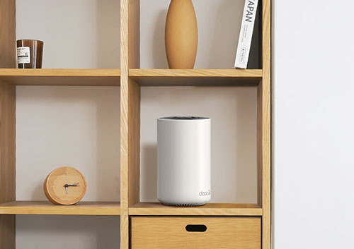 Libreria in legno chiaro con oggetti decorativi: orologio, vaso, libro e cilindro bianco su ripiani e cassetto.