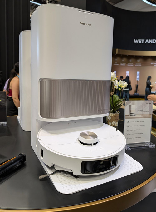 Robot aspirapolvere bianco su base bianca, con stazione di ricarica bianca e dettagli grigi su un tavolo nero.