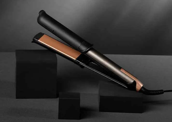 Una piastra per capelli nera e oro su tre blocchi neri, su sfondo grigio scuro.