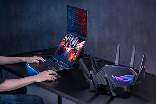Un computer portatile aperto su una scrivania nera, con un router nero con antenne dietro e mani che lo usano.