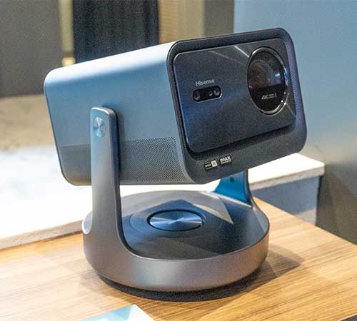 Proiettore grigio e nero su base rotonda, su un tavolo di legno, con sfondo sfocato.