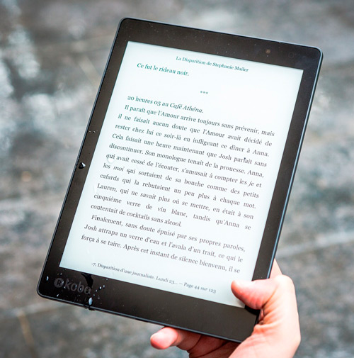 Mano che tiene un tablet nero con testo bianco visualizzato. Lo sfondo � sfocato e neutro.