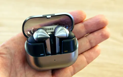 Auricolari argento e neri in custodia aperta, tenuti in una mano su sfondo di legno chiaro.