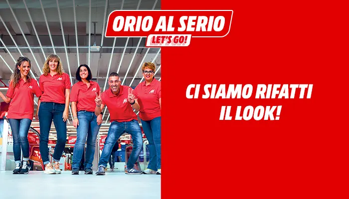 Cinque persone in magliette rosse e jeans davanti a uno sfondo rosso con testo e logo "Orio al Serio Let's Go!".