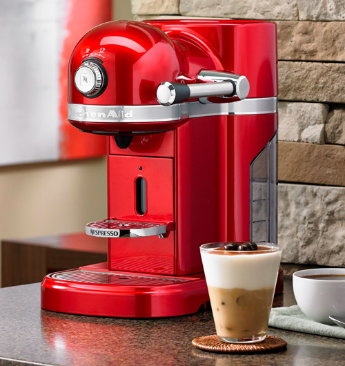 Macchina da caffè rossa con tazza di caffè a strati, su un tavolo con sfondo di muro di pietra.