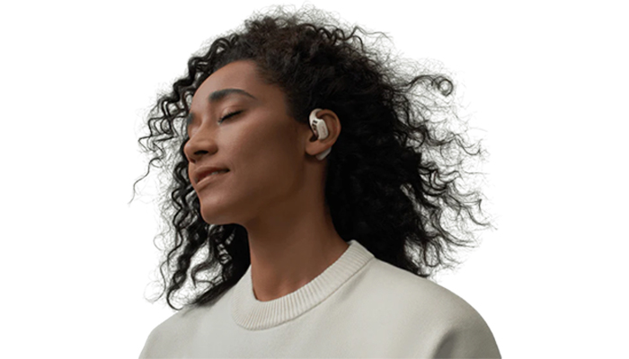 Donna con cuffie bianche, occhi chiusi, indossa una maglietta bianca a maniche lunghe, su sfondo bianco.