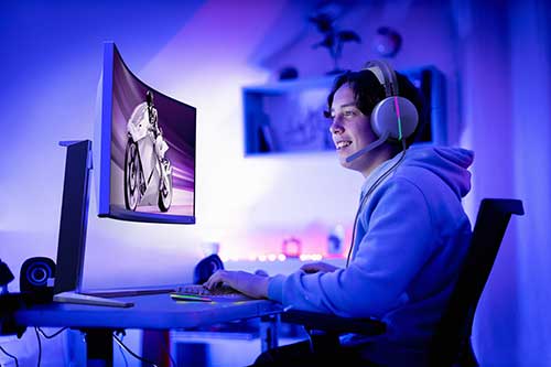 Ragazzo con cuffie gioca al computer. Lo schermo mostra una persona in bici. La stanza � illuminata di blu.