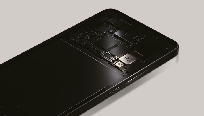 Un telefono nero mostra circuiti interni e componenti su sfondo grigio chiaro.