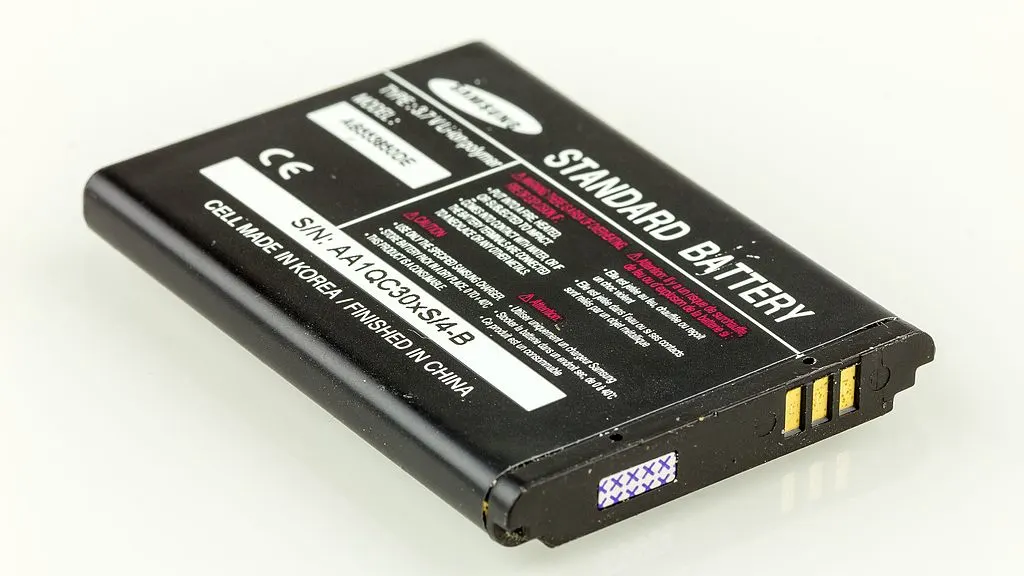 Batteria nera Samsung "Standard Battery" su sfondo bianco. Etichette con avvertenze e specifiche tecniche visibili.