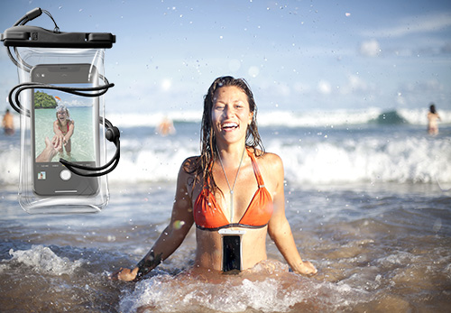 Donna sorridente in bikini arancione, in mare con custodia impermeabile per cellulare in primo piano. Spiaggia e cielo azzurro sullo sfondo.