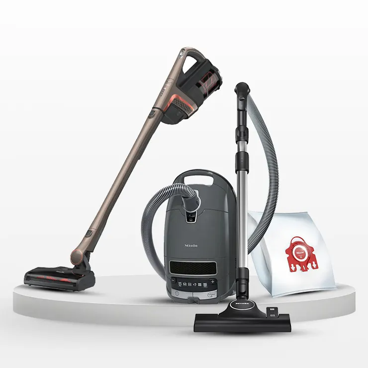 Tre aspirapolveri di colore diverso su una piattaforma bianca con un sacchetto di carta.