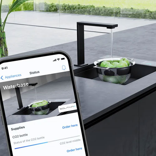 Lavandino nero con frutta verde, rubinetto nero. Un telefono mostra un'app per ordinare una bombola di CO2.